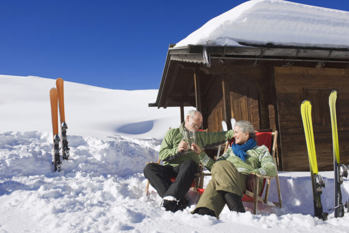Senior couple in front of log cabin, holding champagne glasses