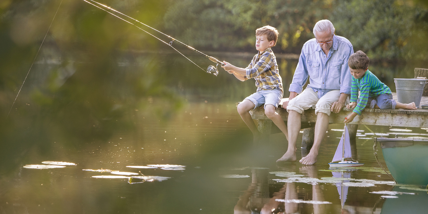 Grandfather and grandsons fishing and playing with toy sailboat at lake