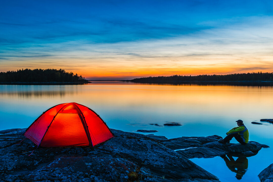 Sunset camping by still Lake Vanern with a tent and a man on a cliff in Sweden